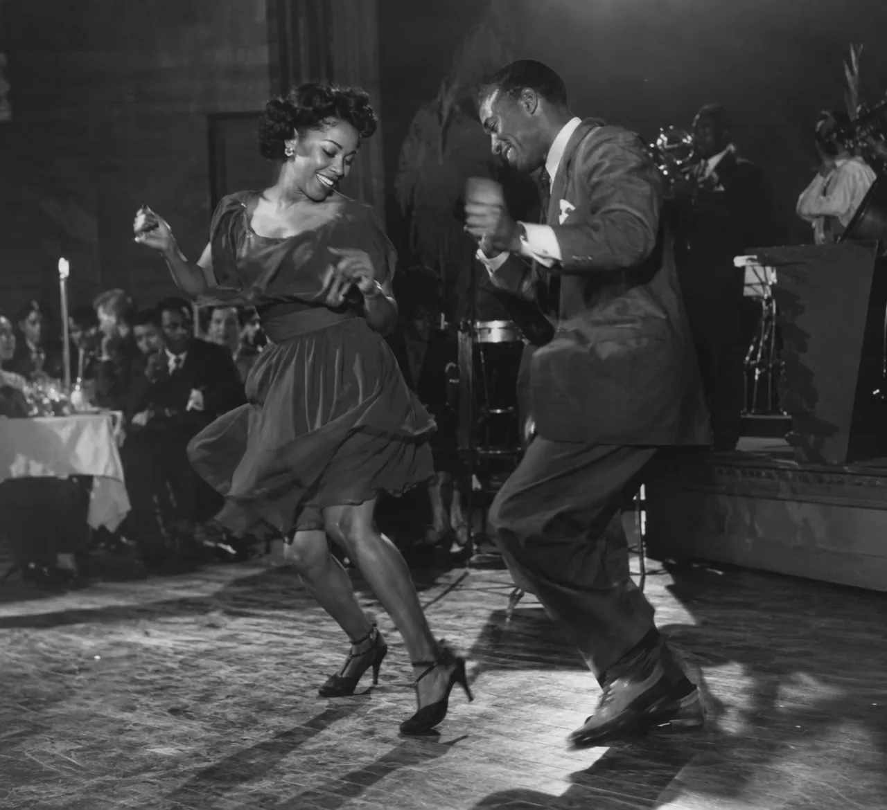 Two dancers improvise jazz steps side by side in front of a band